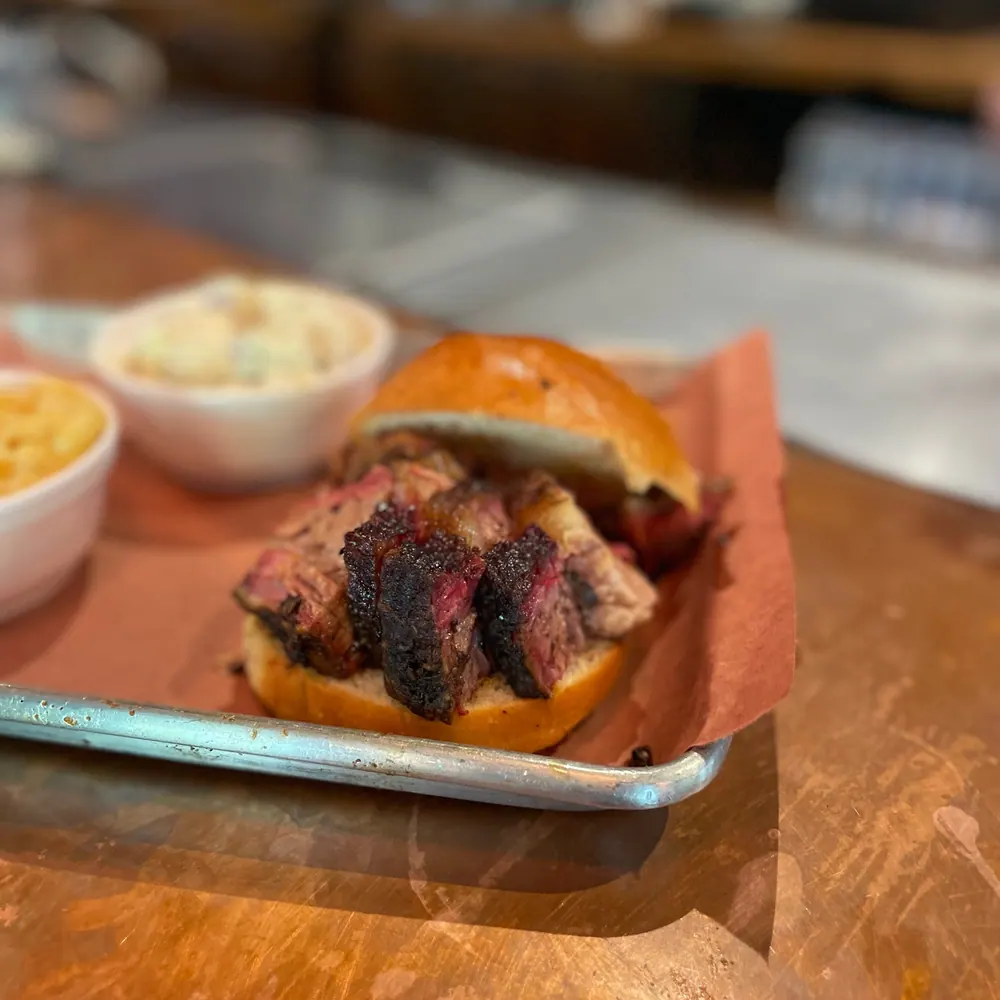 A brisket sandwich on a brioche roll with sides