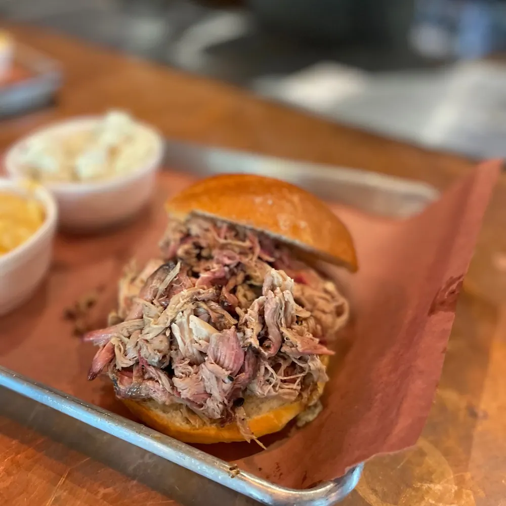 A pulled pork sandwich on a brioche roll with two sides